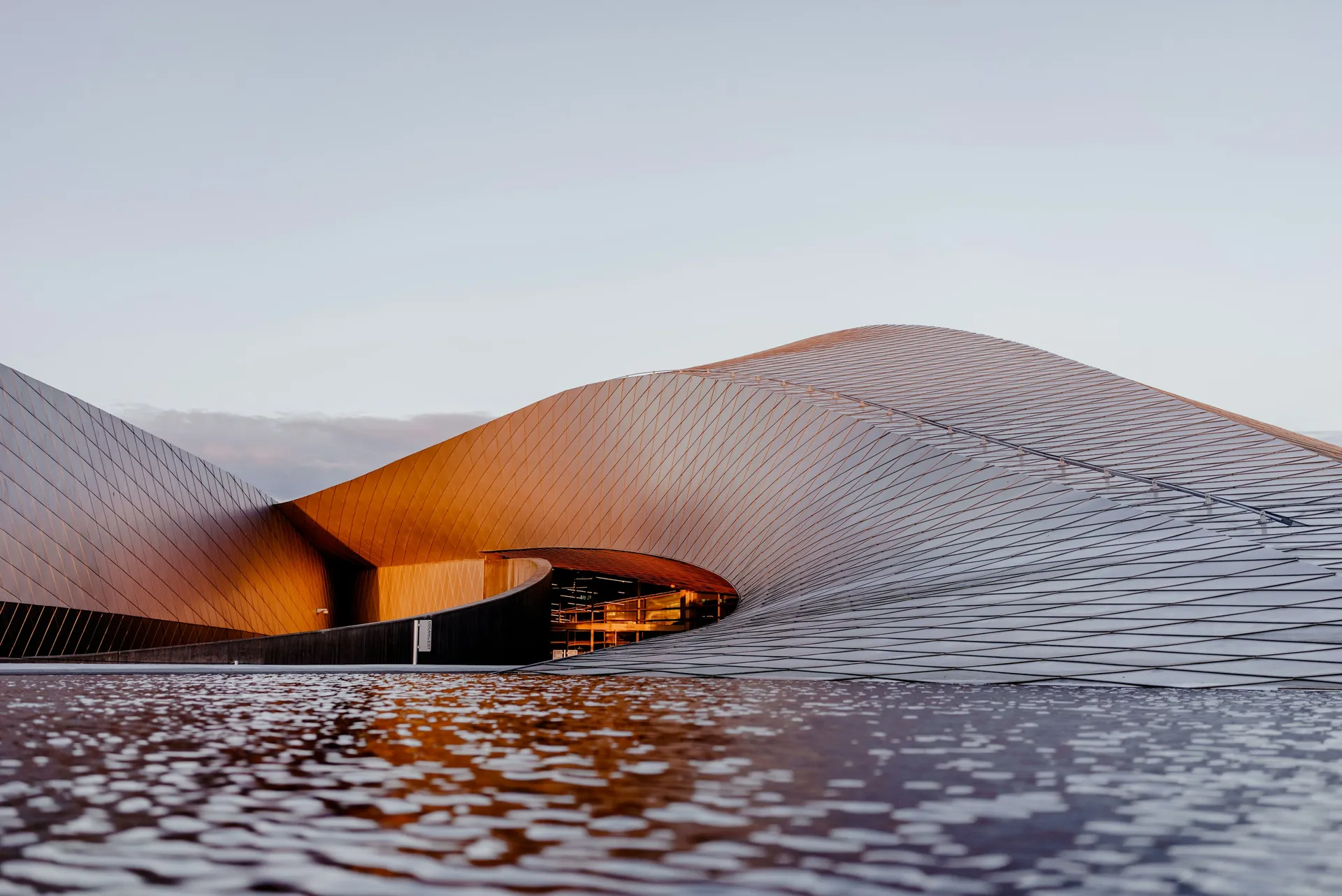 Geschwungene Metallfassade eines modernen Gebäudes am Wasser